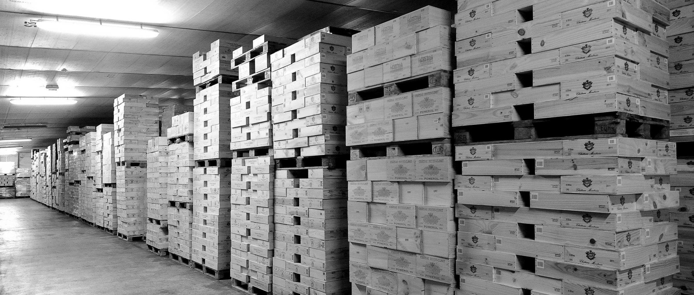 Caisses bois de grands crus empilées dans le chai de Chai des Chartreux, en noir et blanc